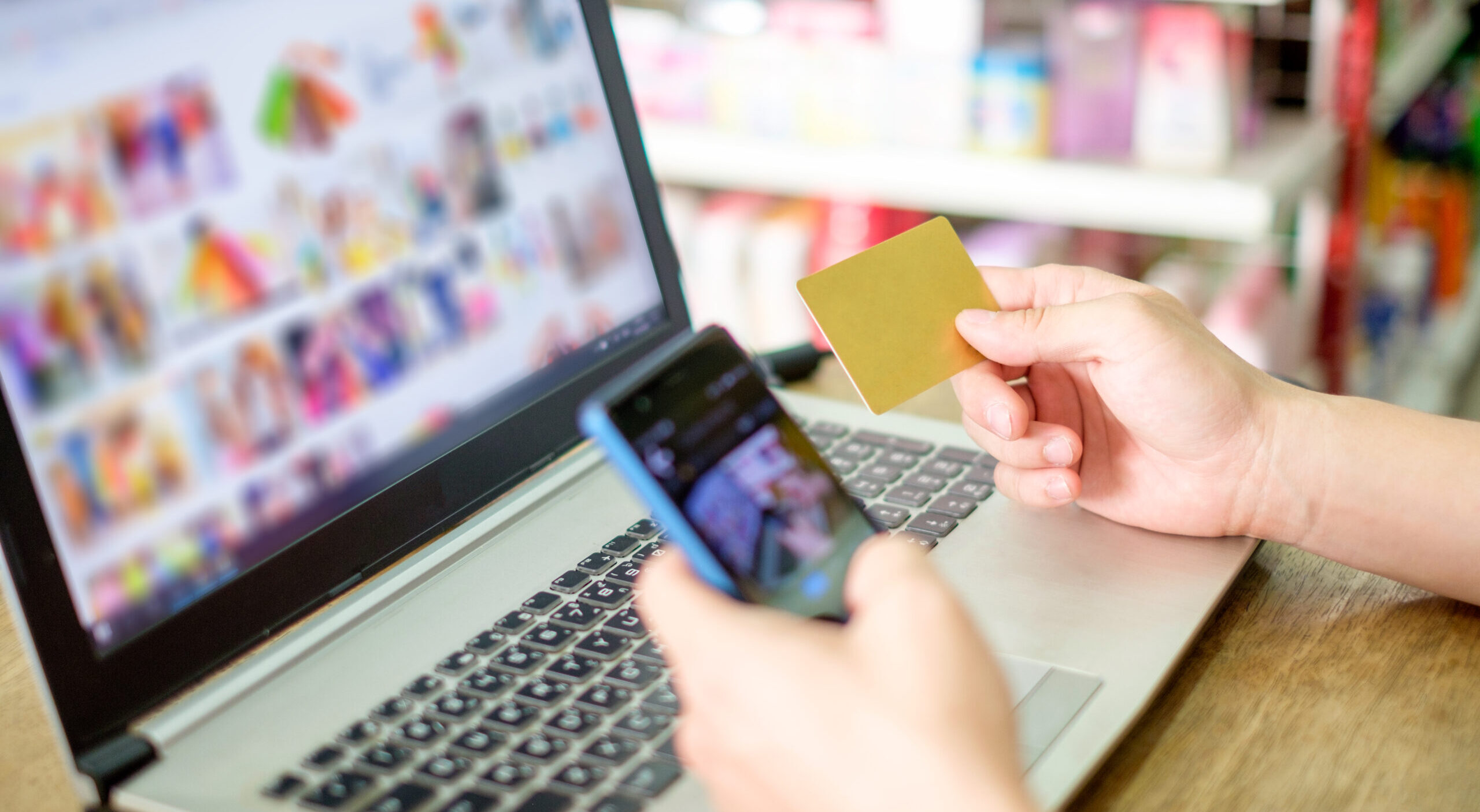 Hand holding credit card and using laptop with smartphone for paying shopping online