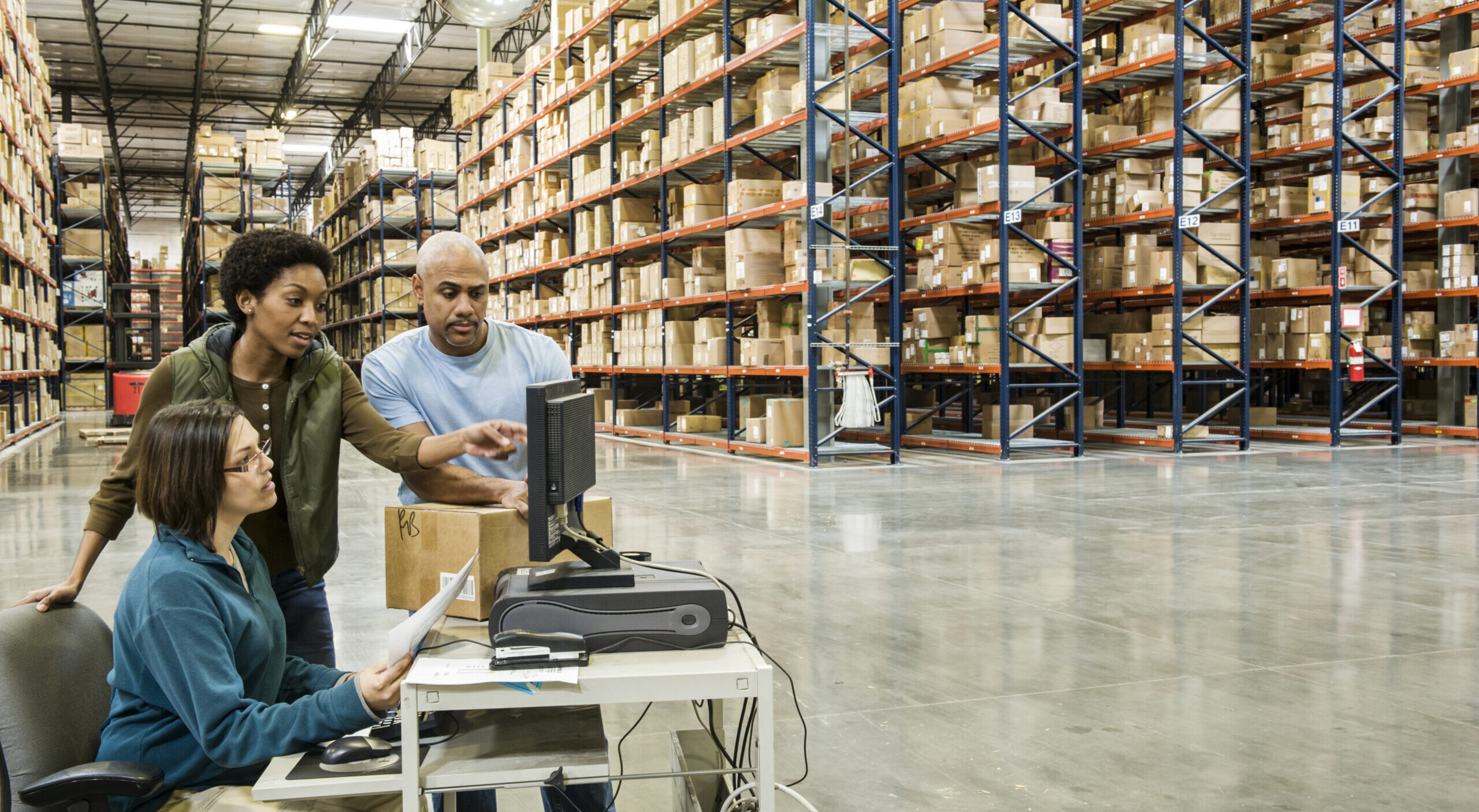Warehouse workers checking inventory on a computer in a large distrubiton warehouse.